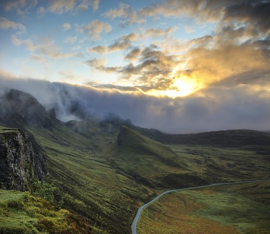 Green mountain valley at sunrise with mist rolling over peaks and a winding road